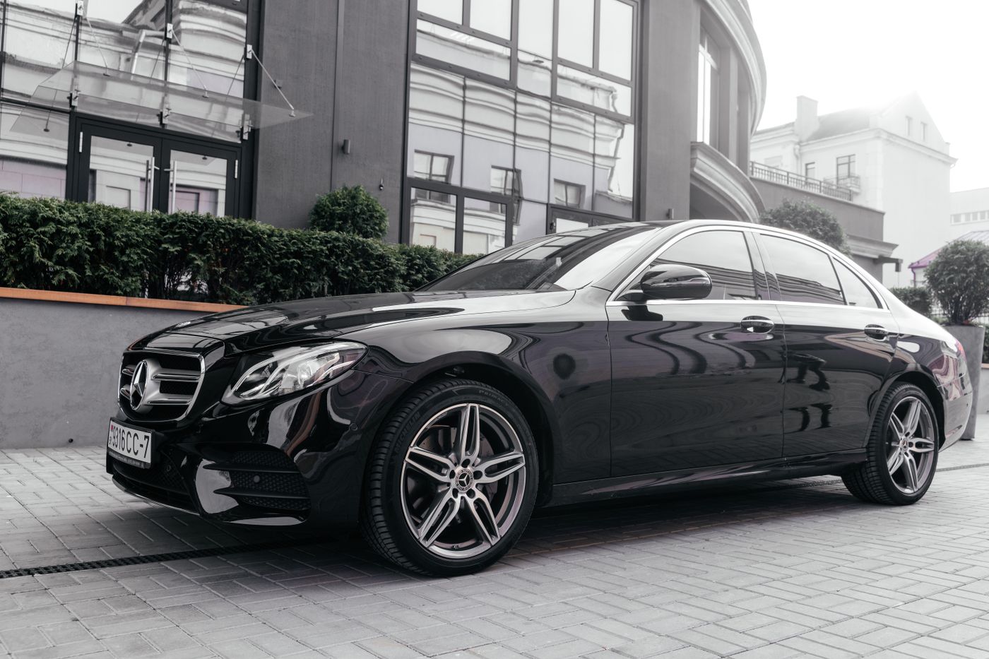 A gloss black Mercedes-Benz E-Class saloon parked outside a modern glass building