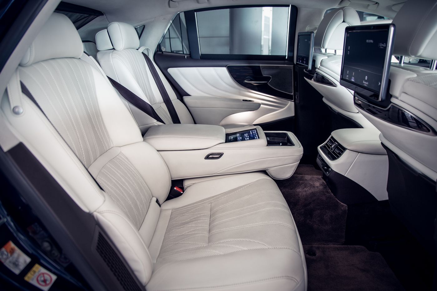 The rear cabin of an executive saloon with cream quilted leather seats and a centre armrest console